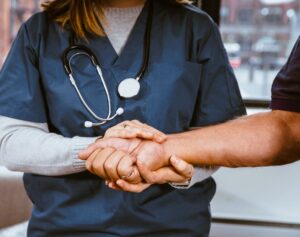 Healthcare worker in blue scrubs with stethoscope holding hand of a patient