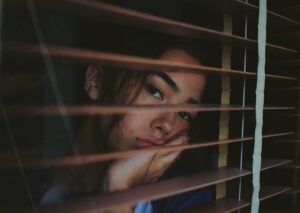 Young Asian woman looking out through window blinds